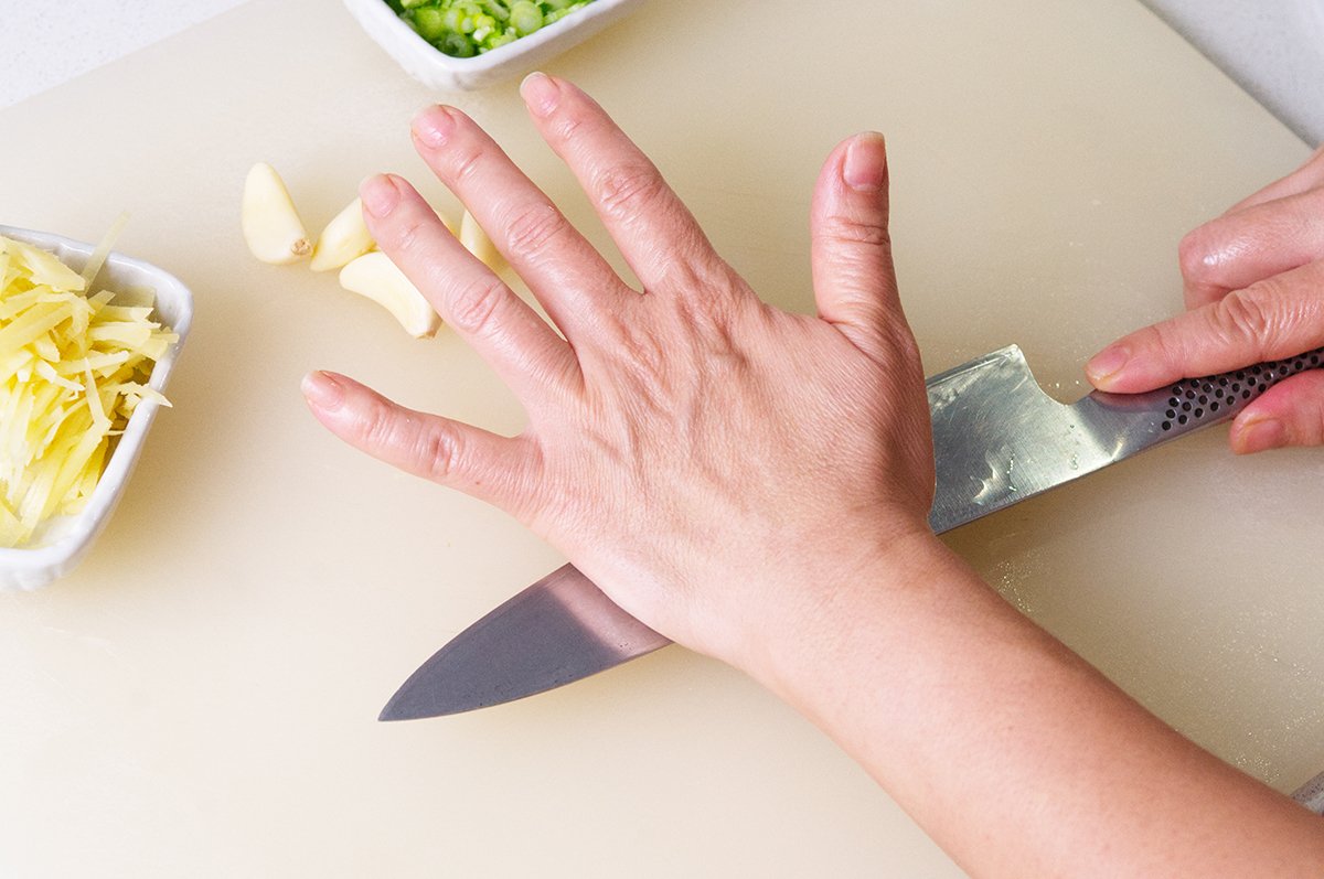 smashing garlic with knife for miso ginger mussels