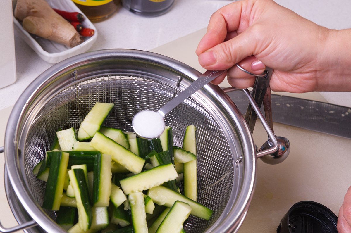 salting szechuan cucumbers in colander